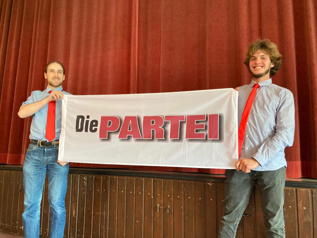 Oliver Boschmann und Yann Caruso halten Die PARTEI Fahne hoch.
