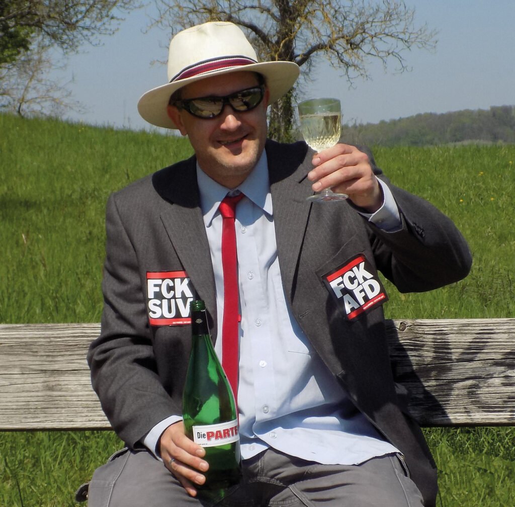 Foto vom Kandidat, rote Krawatte, grauer Anzug, Wein im Glas. 'Bankenviertele